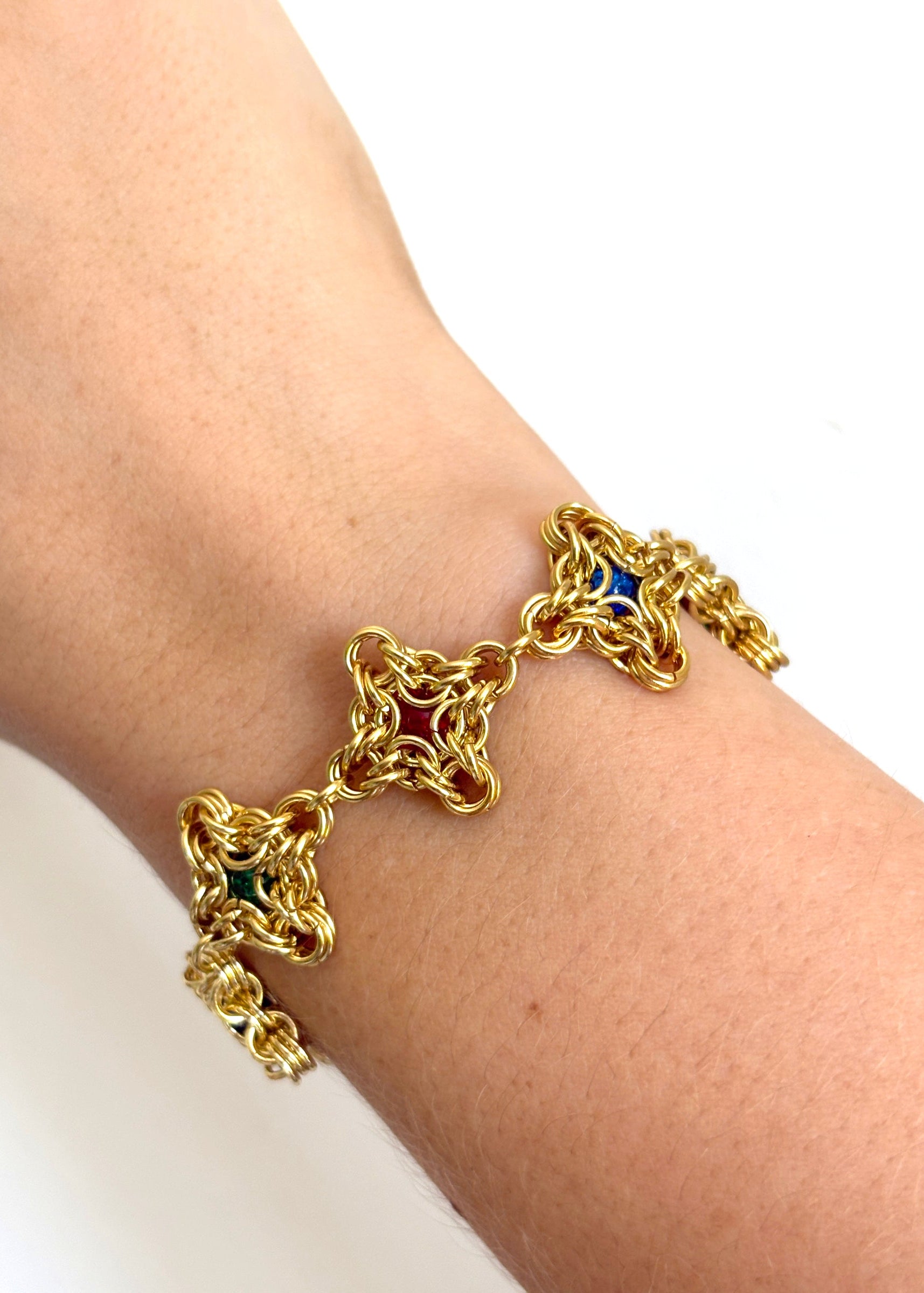 Gold chain bracelet with blue and red stones on a wrist against a white background