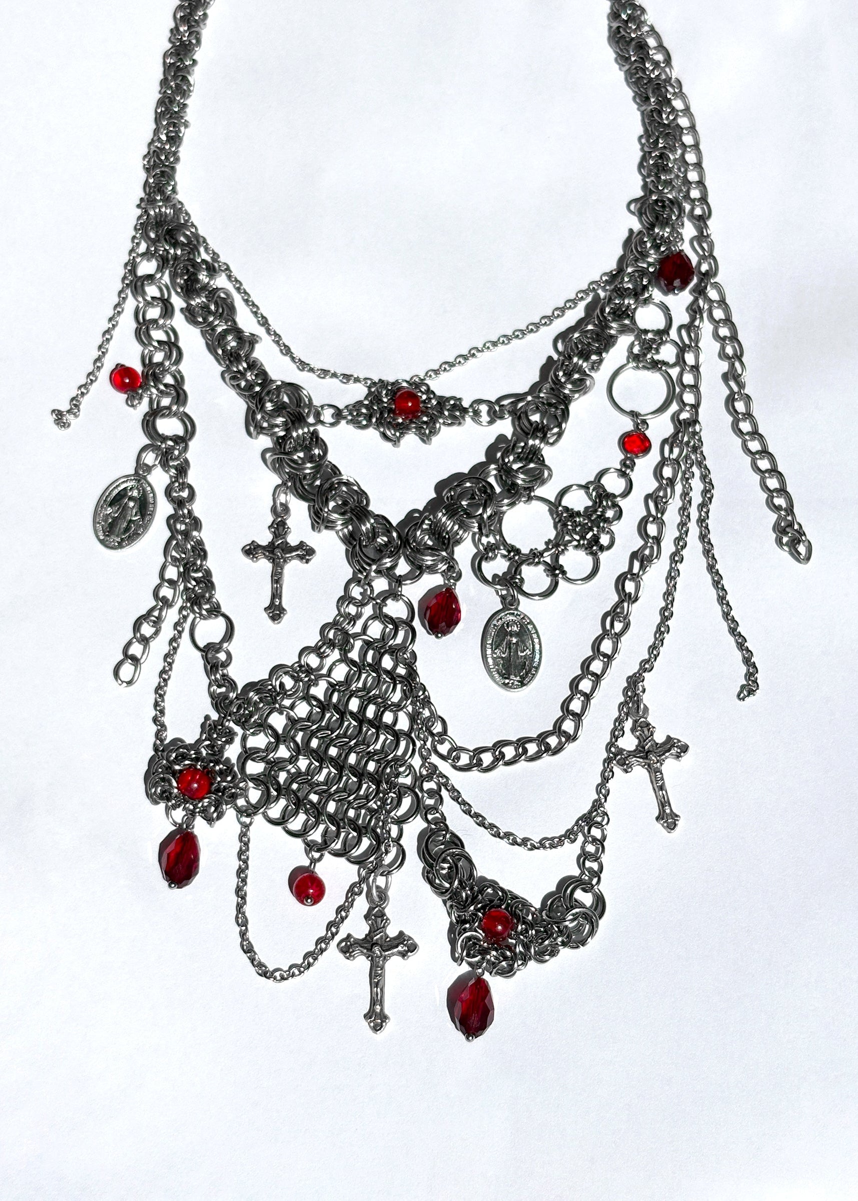 Elaborate necklace with chains, charms, and red stones on a white background